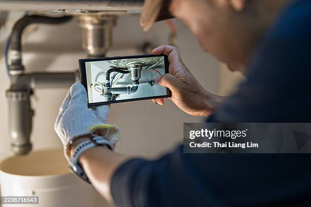 man photographing leaking kitchen sink pipe with smartphone - empreiteiro de reparações imagens e fotografias de stock