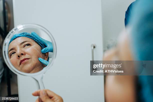 reflexion der reifen frau im spiegel während der kosmetischen facelifting-beratung - schönheitsoperation stock-fotos und bilder