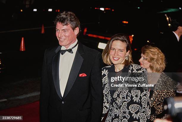 American actor Christopher Reeve, wearing a tuxedo and bow tie, and American actress and singer Dana Morosini, wearing a patterned jacket, attend the...