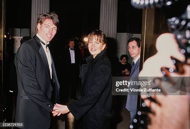 American actor Christopher Reeve, wearing a tuxedo and bow tie, and American actress and singer Dana Morosini, wearing a black overcoat, attending an...