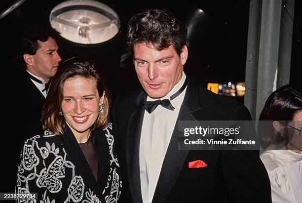 American actor Christopher Reeve, wearing a tuxedo and bow tie, and American actress and singer Dana Morosini, wearing a patterned jacket, attend the...