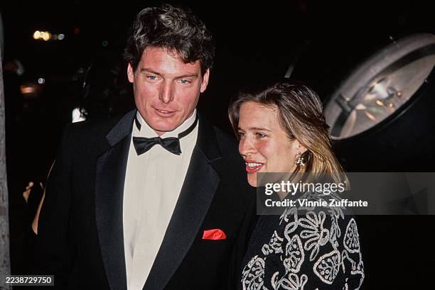 American actor Christopher Reeve, wearing a tuxedo and bow tie, and American actress and singer Dana Morosini, wearing a patterned jacket, attend the...