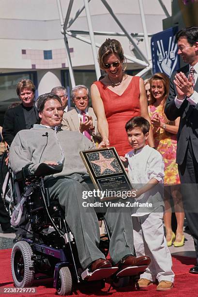 American actor Christopher Reeve, wearing a grey sweater and grey trousers, with his wife, American actress and singer Dana Reeve, and their son,...