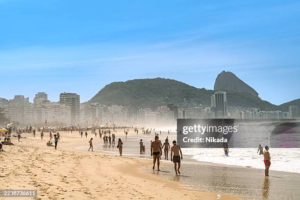 soleada playa de río con costa abarrotada y pan de azúcar en río de janeiro, brasil - playa de copacabana fotografías e imágenes de stock
