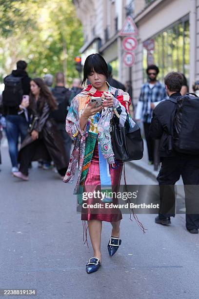 Susie Lau wears straight black hair with bangs, chin-length, a black leather shoulder bag, a white printed T-shirt with a multicolor graphic under a...