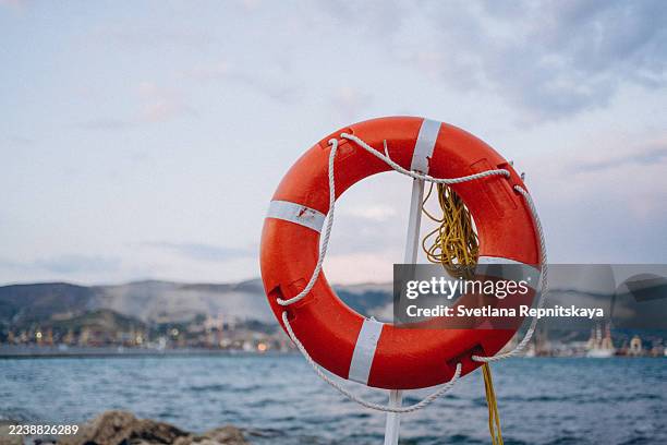 orange lifebuoy providing safety at sea with port view - nautische ausrüstung stock-fotos und bilder