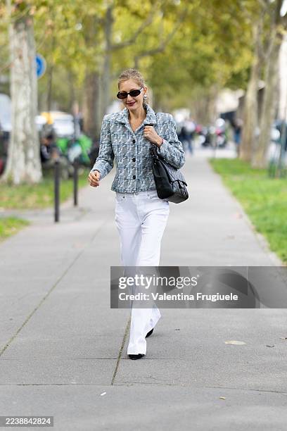 Guest wears black sunglasses, a grey polo tweed jacket, a black leather Chanel bag, white high waist denim trousers and black shoes outside Rabanne...