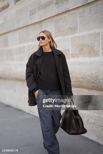 Claire Rose Cliteur is seen wearing a dark brown crewneck knit sweater layered under a dark brown short oversized button-up coat with a boxy...
