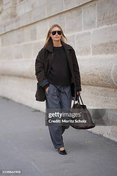 Claire Rose Cliteur is seen wearing a dark brown crewneck knit sweater layered under a dark brown short oversized button-up coat with a boxy...