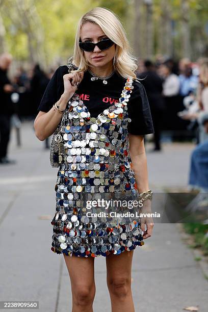 Guest wears black graphic pattern t-shirt, silver big sequins mini dress, silver metallic Rabanne bag, black sunglasses, outside Rabanne, during the...
