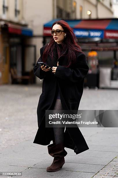 Guest wears black tights, brown suede boots, brown sunglasses and a black oversized coat outside Issey Miyake show during the Womenswear Spring...