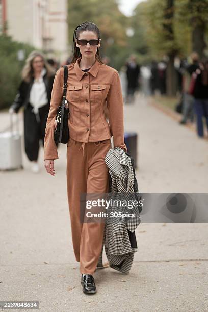 Libby Taverner is seen wearing her hair slicked back, rectangular dark sunglasses, a fitted terracotta buttoned jacket, matching wide-leg trousers,...