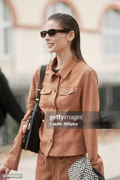 Libby Taverner is seen wearing her hair slicked back, rectangular dark sunglasses, a fitted terracotta buttoned jacket, matching wide-leg trousers,...