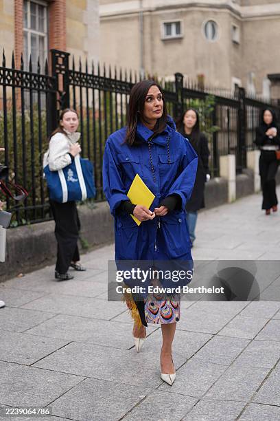 Guest wears straight shoulder-length dark brown hair with a center part, a yellow Loewe invitation, an oversized cobalt blue hooded parka jacket with...