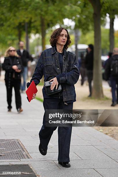 Guest wears shoulder-length curly brown hair with a middle part, gold rings on a hand holding a bag, a black leather top-handle bag with flap and...