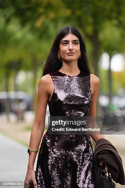 Guest wears long, straight, dark brown hair with a center part, gold-tone drop earrings with red stones and a gold-tone bracelet with a green stone...