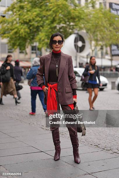Guest wears black sunglasses, a neon red turtleneck pullover, a red pullover knit at the waist, a brown turtleneck t-shirt, a pale brown blazer...