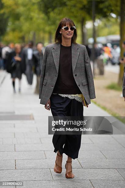 Guest is seen wearing a single-breasted structured checked blazer in grey, worn draped over the shoulders; a dark brown crewneck sweater with ribbed...