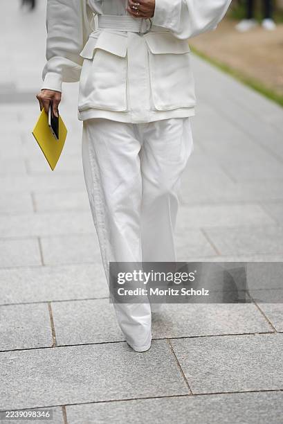 Christine Centenera is seen wearing a long-sleeved, ivory belted utility-style jacket with a structured silhouette, emphasized cuffs, flap pockets on...