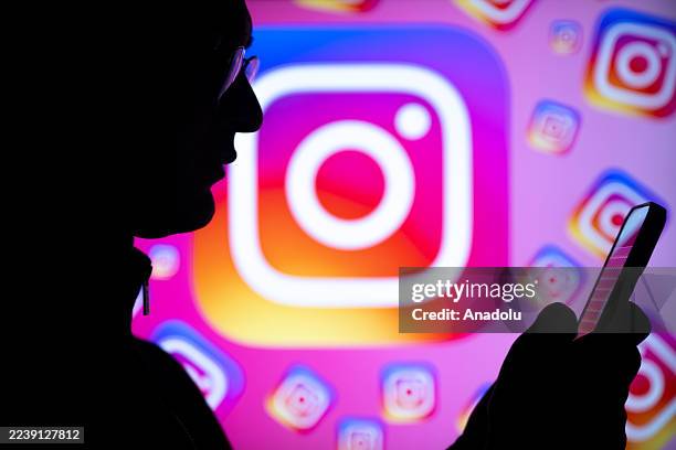 Person is looking at a phone screen in front of a screen displaying the logos of Instagram in Ankara, Turkiye on October 03, 2025.