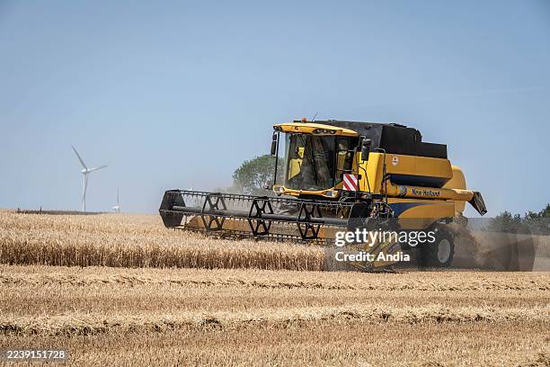 Pere-Saint-Pierre-la-Noue, Aunis plain : a combine harvester in a barley field in front of wind turbines under the June sun, as harvesting gets off...