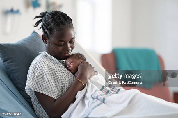black mother cradling newborn baby in hospital bed during postpartum moment - real family stock pictures, royalty-free photos & images