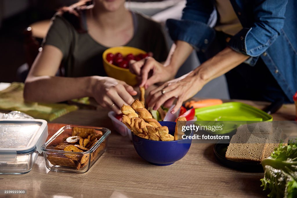 Friends and family preparing snacks at a table with bread, chips and fresh vegetables together