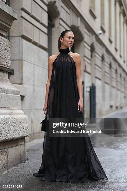 Danielle Copperman wears a slicked-back low ponytail, dark brown, long, gold hoop earrings, a small black leather top-handle bag, a sheer black...