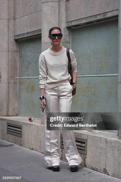 Guest wears a pulled-back low ponytail in dark brown hair with a center part, oversized black shield sunglasses, stacked bracelets including a large...