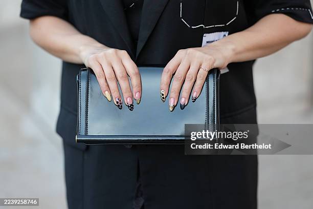 Samia Laaboudi wears a black varnished leather clutch bag, a short-sleeve black knit top, an oversized black sleeveless blazer jacket-style vest with...