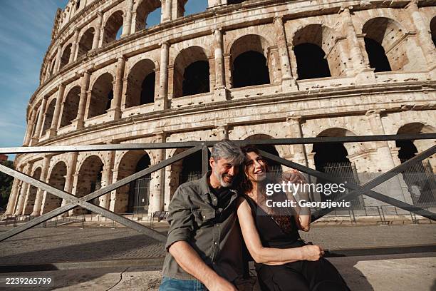 senior tourists smiling in front of the colosseum - coliseum rome stock pictures, royalty-free photos & images