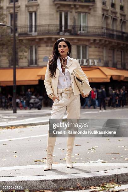 Farnoush Hamidian wears an ivory tailored jacket with a white shirt, cream trousers tucked into beige boots, accessorized with gold jewelry, a...