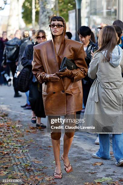 Guest wears brown oversize leather hooded blazer with gloves attached, matching capri pants, brown sandals, olive green Bottega Veneta bag, brown...