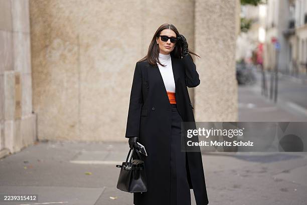 A guest is seen wearing a full Look from Hermes including a long black wool coat with a tailored cut, double breasted front and minimal detailing; a...
