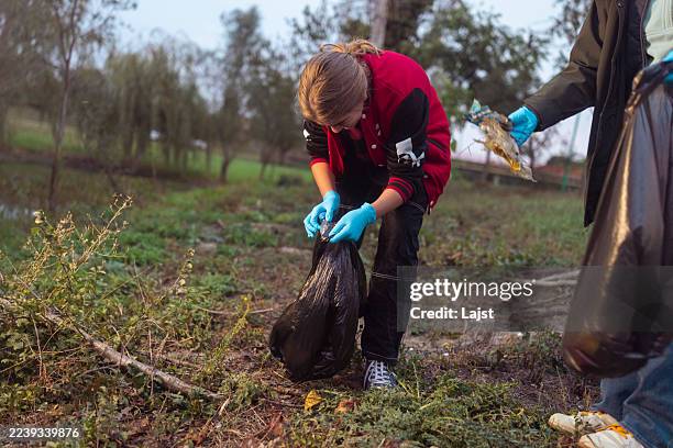 teen girl wearing gloves collecting trash outdoors in natural setting at dusk - initiative stock pictures, royalty-free photos & images