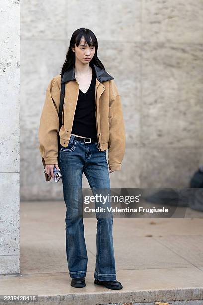 Model wears a black v-neck tank top, a beige blazer, a black belt, blue low waist jeans, black leather shoes and a black leather crossbody bag...