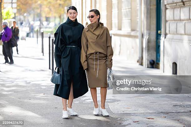 Amalie Gassmann wears black belted coat, blue bag & Ginevra Mavilla wears brown skirt, jacket, silver bag, white heels, sunglasses outside Lacoste...