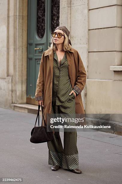 Olha Naumova wears silk green with brown pattern set made of pants and shirt, brown long trench coat, green flats, brown head scarf, brown sunglasses...