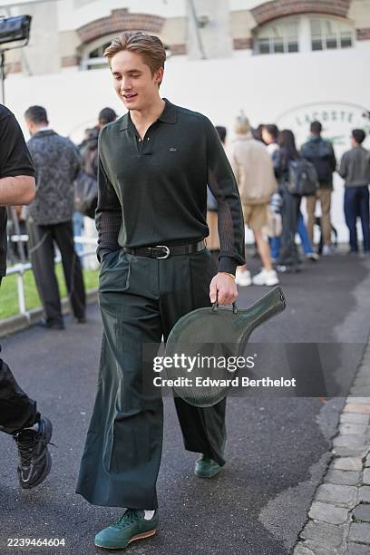 Guest wears short swept-back light brown hair, a small gold hoop earring and a gold chain bracelet, a dark green croc-embossed leather bag in shape...