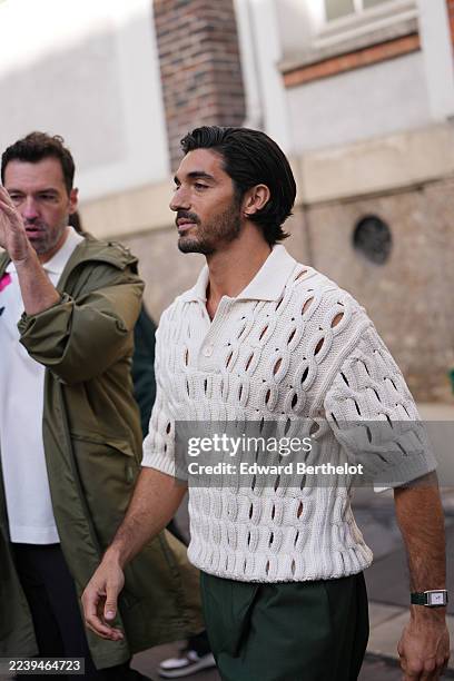 Taylor Zakhar Perez wears medium-length dark brown hair slicked back, a silver rectangular watch with a black strap, an ivory open-knit short-sleeve...