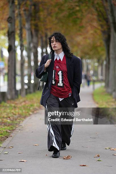 Guest wears shoulder-length curly black hair with a center part, a green leather shoulder bag, a navy blazer jacket, a white collared shirt layered...