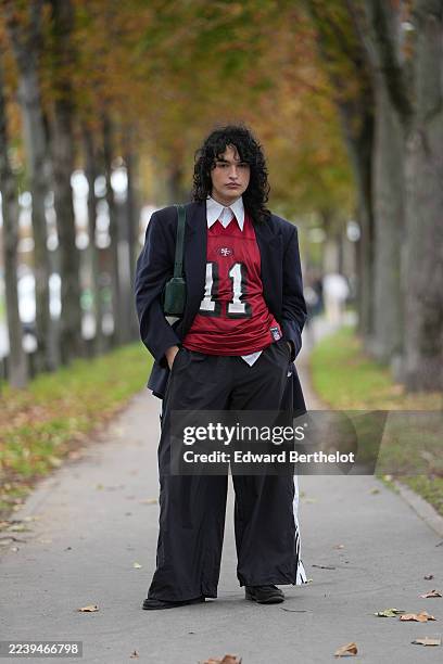 Guest wears shoulder-length curly black hair with a center part, a green leather shoulder bag, a navy blazer jacket, a white collared shirt layered...