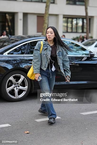 Guest wears long straight black hair with a center part, silver hoop earrings and silver rings, a yellow fabric shoulder bag, an oversized blue denim...