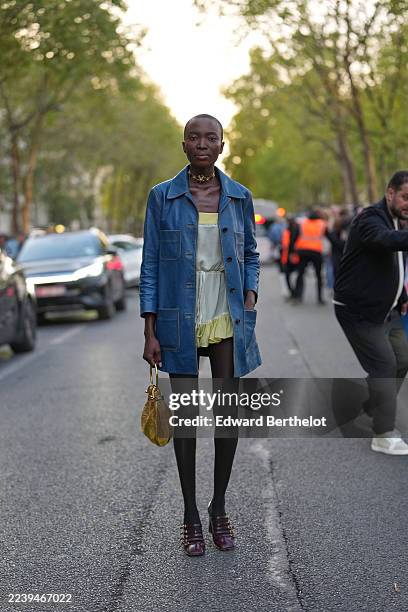 Guest wears a shaved close-cropped black hairstyle, a gold choker necklace, a yellow textured leather top-handle bag from Chloe with gold hardware, a...