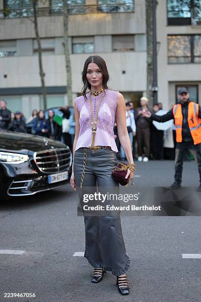 Guest wears long dark brown hair worn loose with a center part, layered gold-tone jewelry including a chunky gold choker with black bead accents, a...