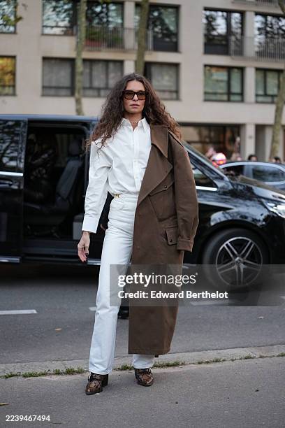 Guest wears long dark brown curly hair parted in the center, rectangular tortoiseshell brown sunglasses, a thin gold chain necklace, a white...
