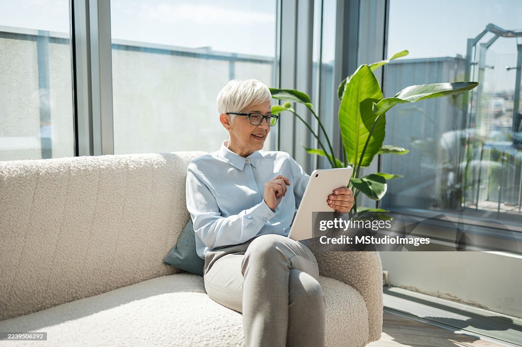 Smiling senior woman using a tablet while sitting on a sofa