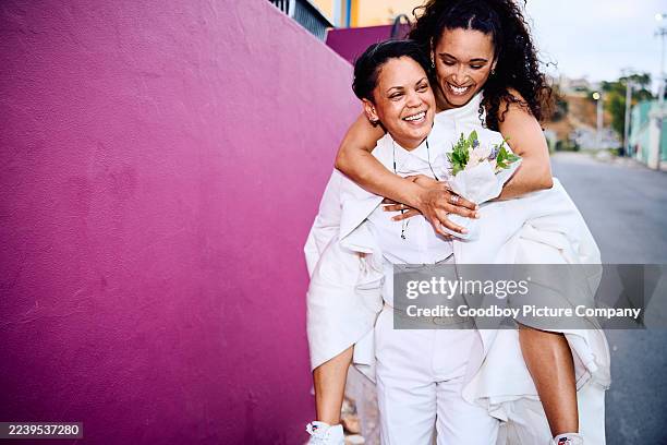pareja queer feliz compartiendo un paseo a caballito al aire libre junto a un audaz muro magenta el día de su boda - queer fotografías e imágenes de stock