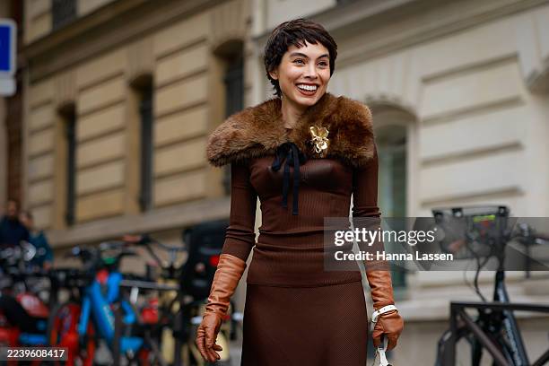 Fer Millán is seen wearing brown top, brown fur collar, gold flower brooch, brown midi skirt, brown socks, black sandals, white Miu Miu bag and camel...
