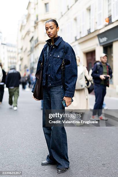 Model wears a dark indigo corduroy jacket with matching wide-leg jeans, black shoes, and a brown tote bag outside Sacai show during the Womenswear...